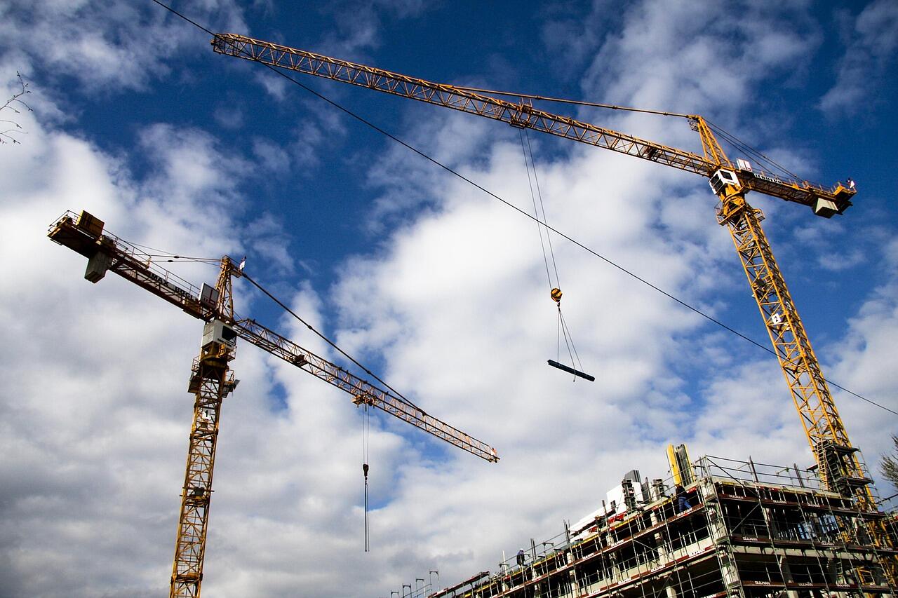 Tower cranes standing over a construction site under a bright sky